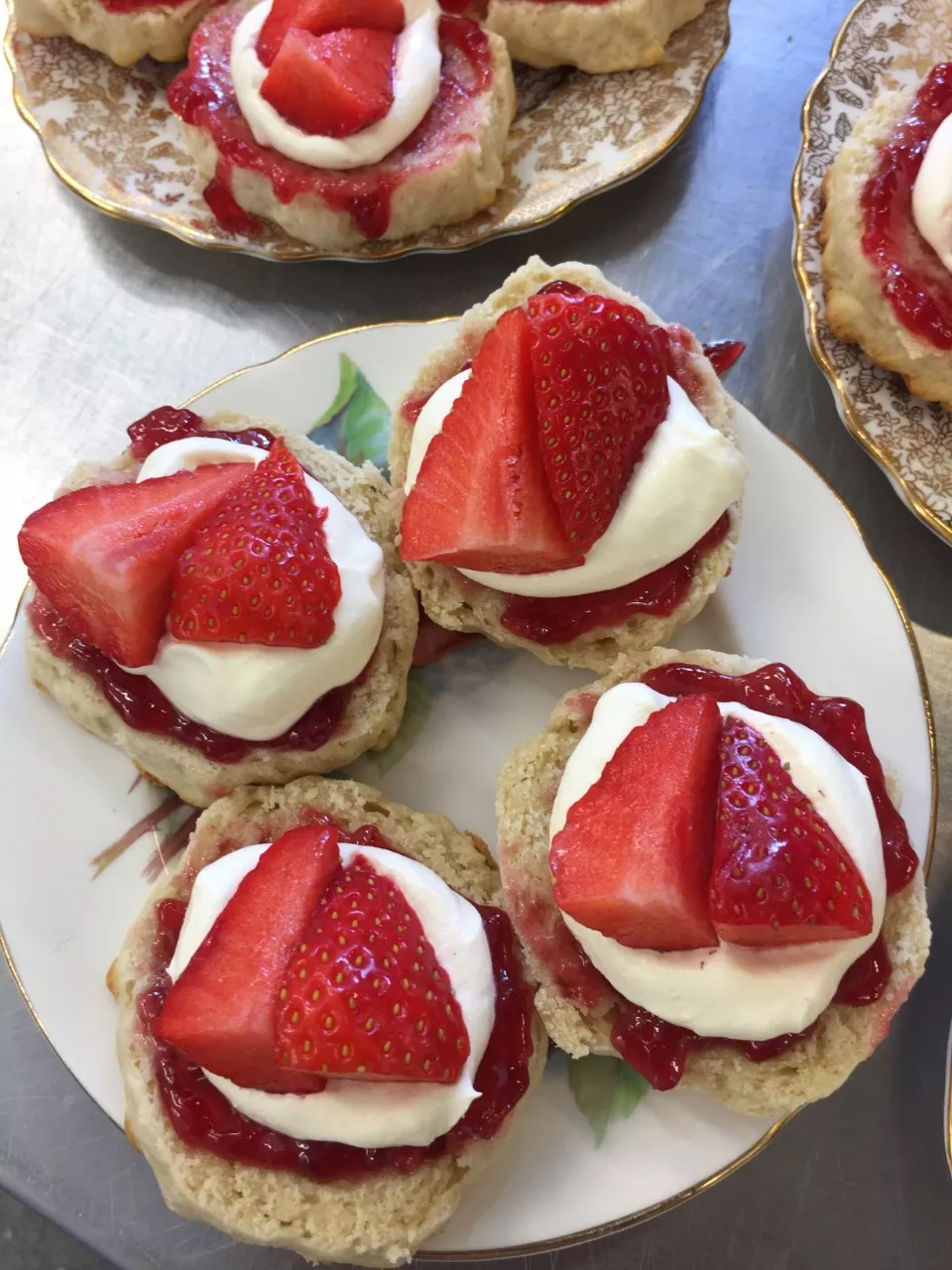 http://Four%20classic%20cream%20tea%20scones%20with%20jam,%20cream%20and%20fresh%20strawberries%20on%20top%20on%20a%20pretty%20vintage%20plate.